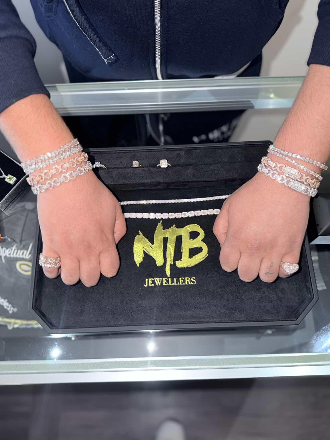 Hands wearing diamond bracelets and rings over an NTB Jewellers tray